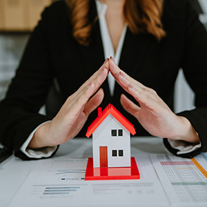 Hands forming a roof over a model house; legal asset protection and real estate planning services.